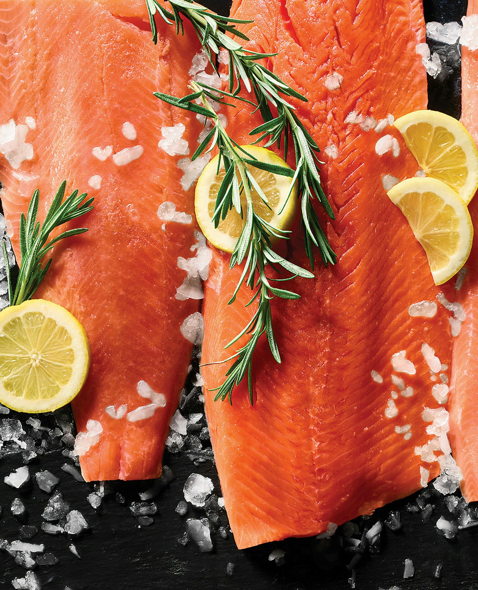 Raw salmon filets with lemon slices, rosemary, and sea salt sprinkles